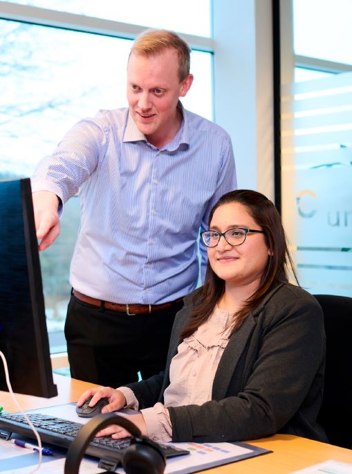 Indkøbselev Zaina sidder foran sin computer og får vejledning af en mand på virksomheden Unicon i Vejle